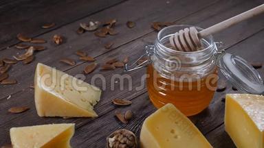 奶酪和蜂蜜。 各种各样的硬奶酪都在木制背景上。 蜂蜜在蜂蜜棒上。 慢动作